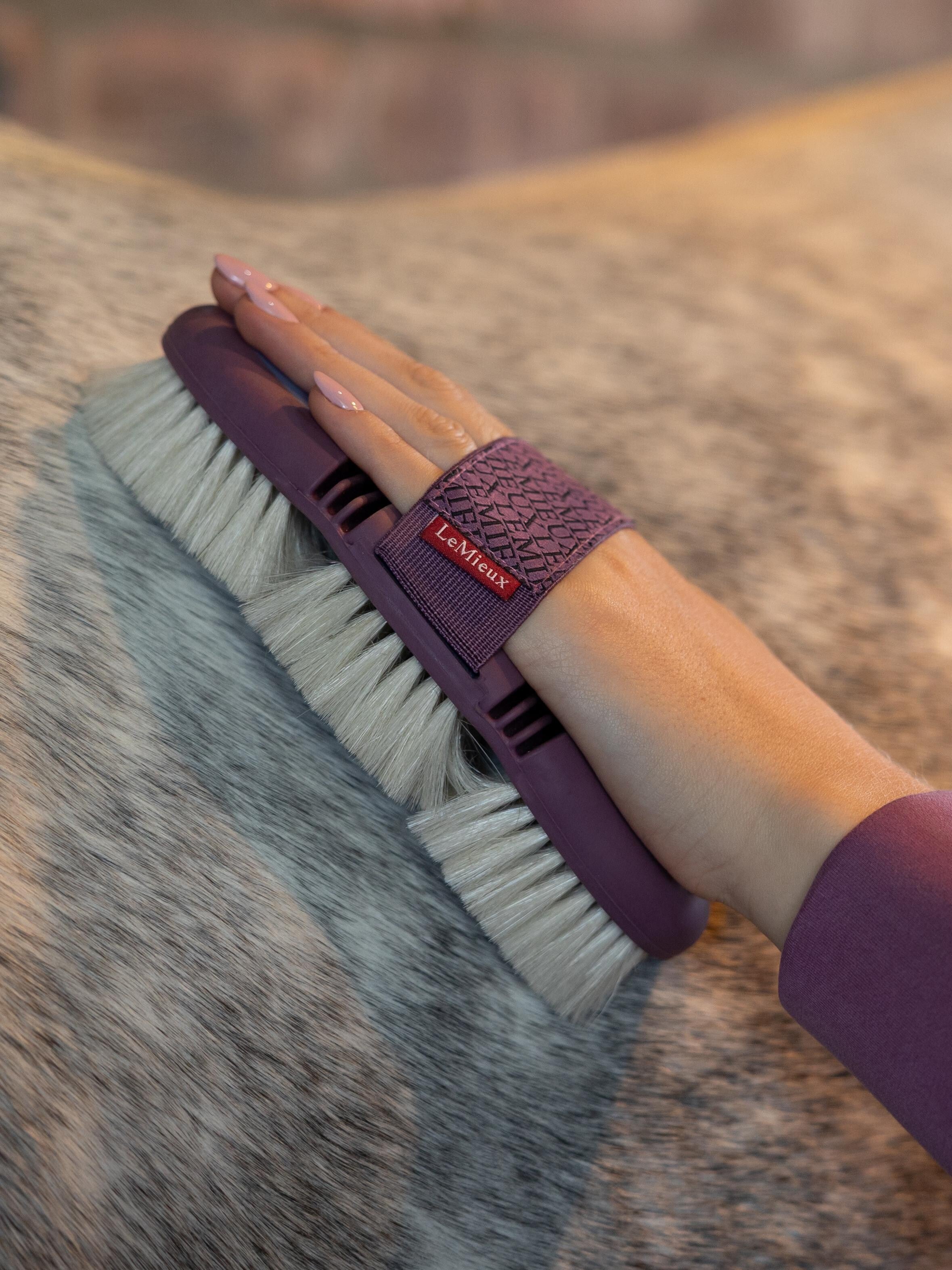 Close up view of a woman grooming a gray horse with the Lemieux Flexi Goats Hair Body Brush in purple and light blue with cream colored bristles