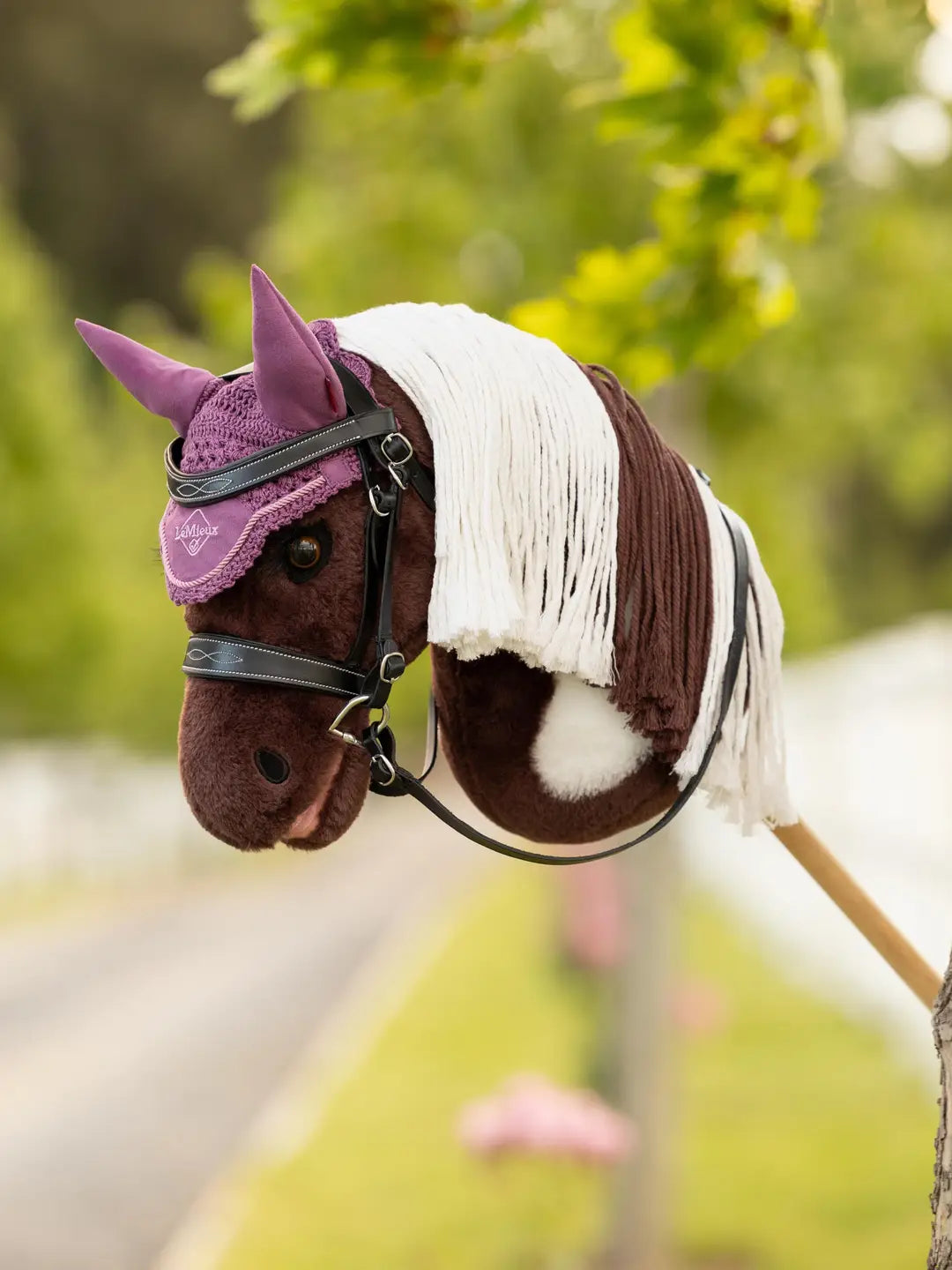 Angled front view of a paint hobby horse wearing the pink LeMieux Hobby Horse Ear Bonnet outside