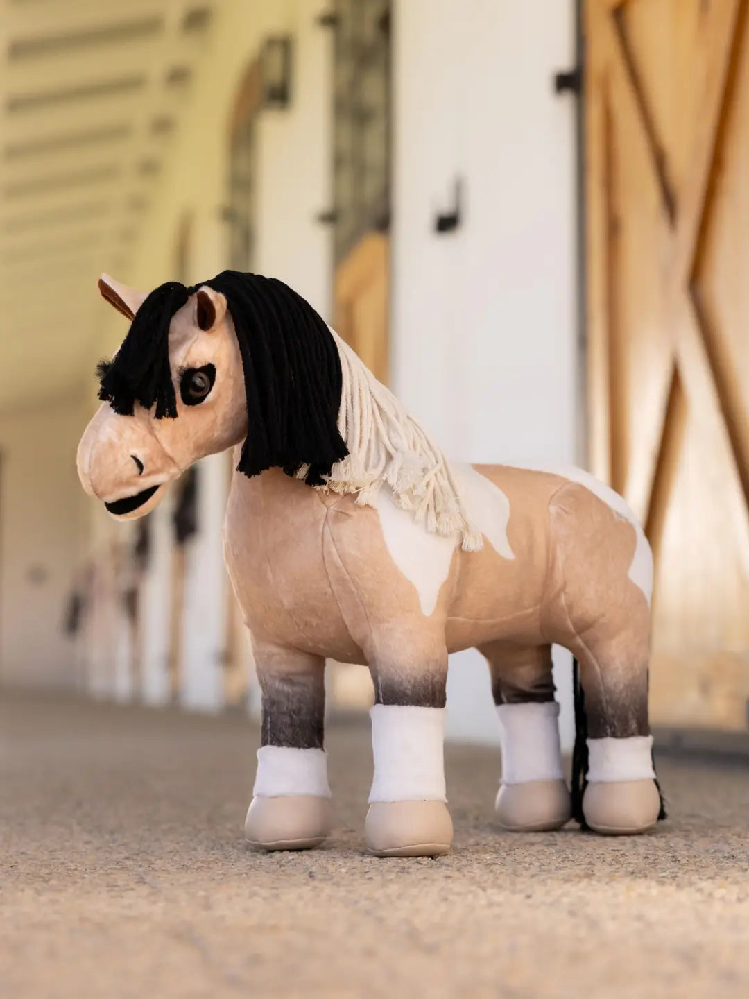 A buckskin paint stuffed animal horse standing in a barn aisle