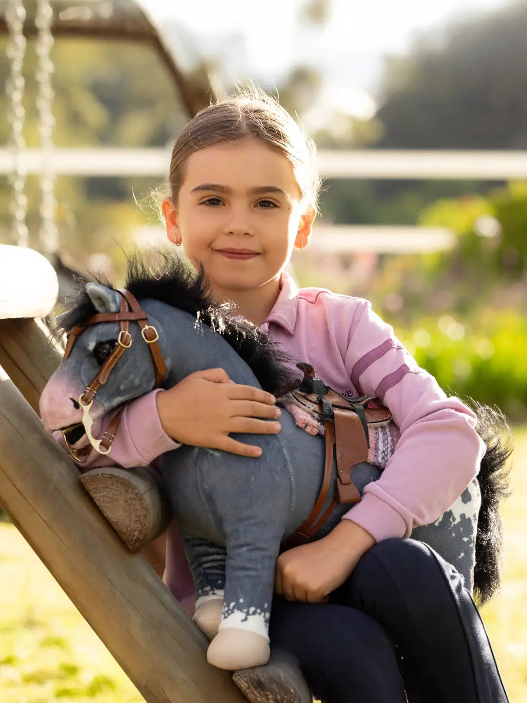 A young girl sitting down holding a gray appaloosa stuffed animal horse