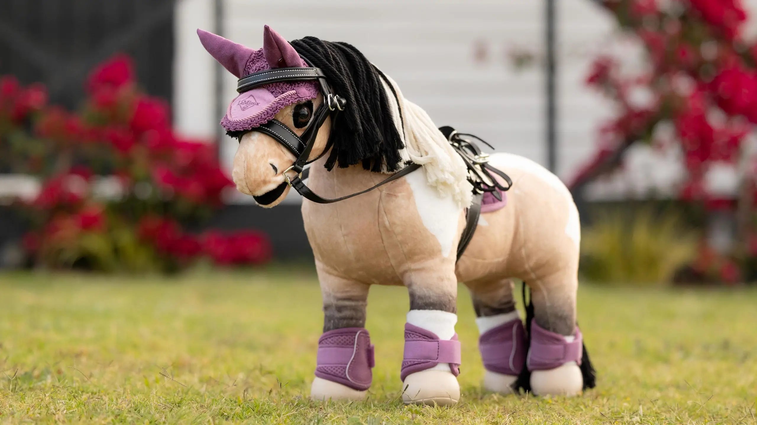 Angled front view of a buckskin paint wearing the pink LeMieux Toy Pony Fly Hood and matching set while standing in the grass