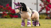 Angled front view of a buckskin paint wearing the pink LeMieux Toy Pony Fly Hood and matching set while standing in the grass