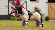 Side view of a buckskin paint wearing the pink LeMieux Toy Pony Saddle Pad while standing in the grass