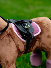 Angled front view of a brown toy pony wearing the pink LeMieux Toy Pony Saddle Pad while standing in the grass