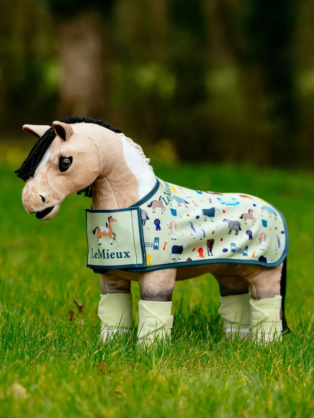 A stuffed animal horse standing outside wearing the LeMieux Toy Pony Printed Fleece Rug in green