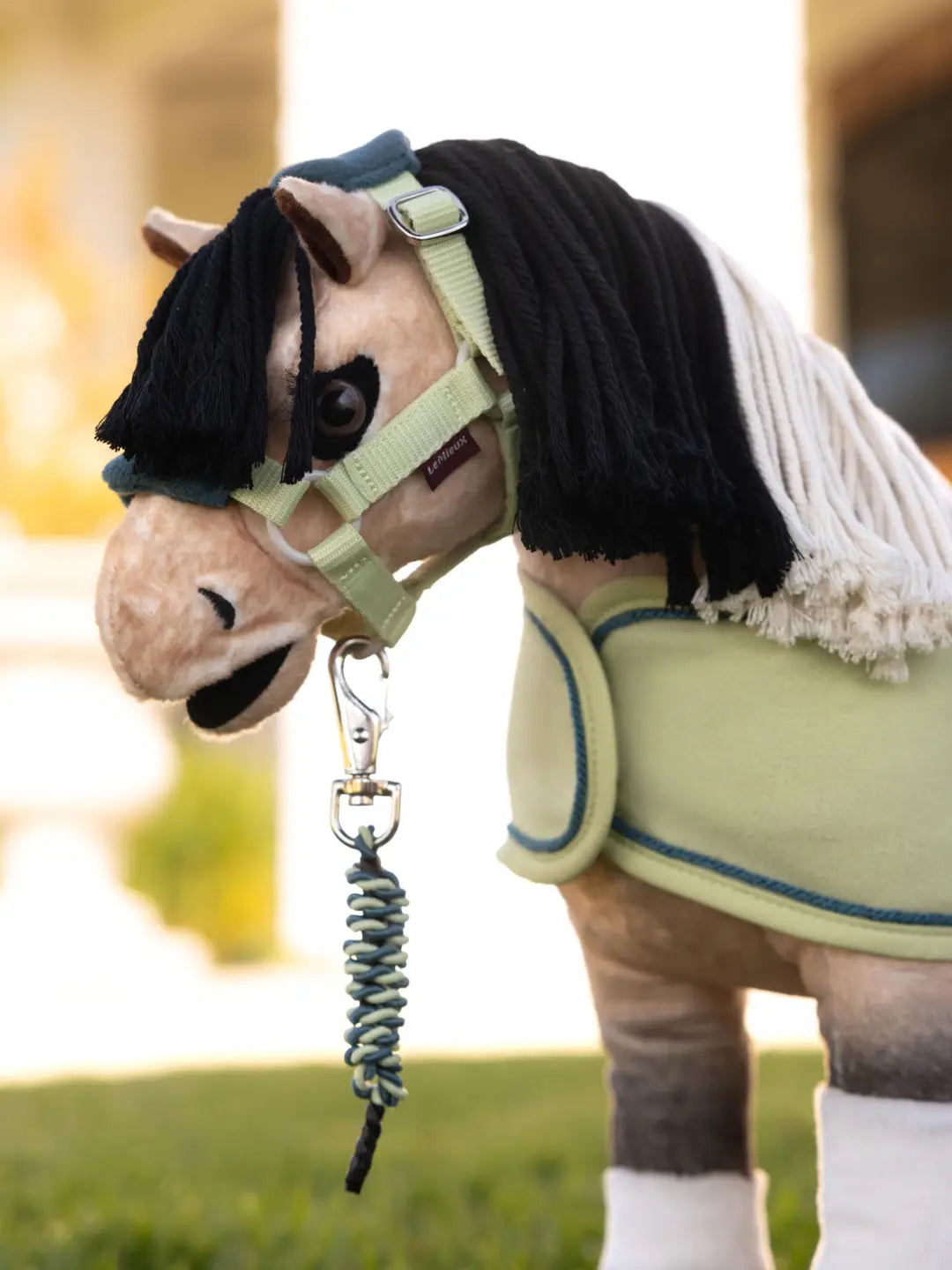 A stuffed animal toy horse standing outside wearing the Toy Pony Vogue Headcollar & Leadrope in green and blue