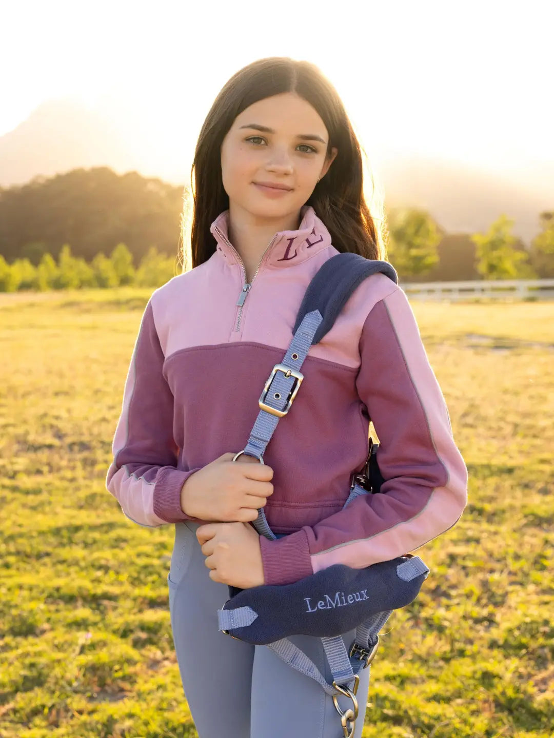 Front view of a young female model wearing the pink LeMieux Young Rider Cropped Kate Quarter Zip while standing outside