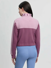 Back view of a young female model wearing the pink LeMieux Young Rider Cropped Kate Quarter Zip on a plain background