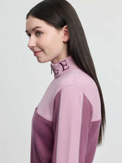 Side view of a young female model wearing the pink LeMieux Young Rider Cropped Kate Quarter Zip on a plain background