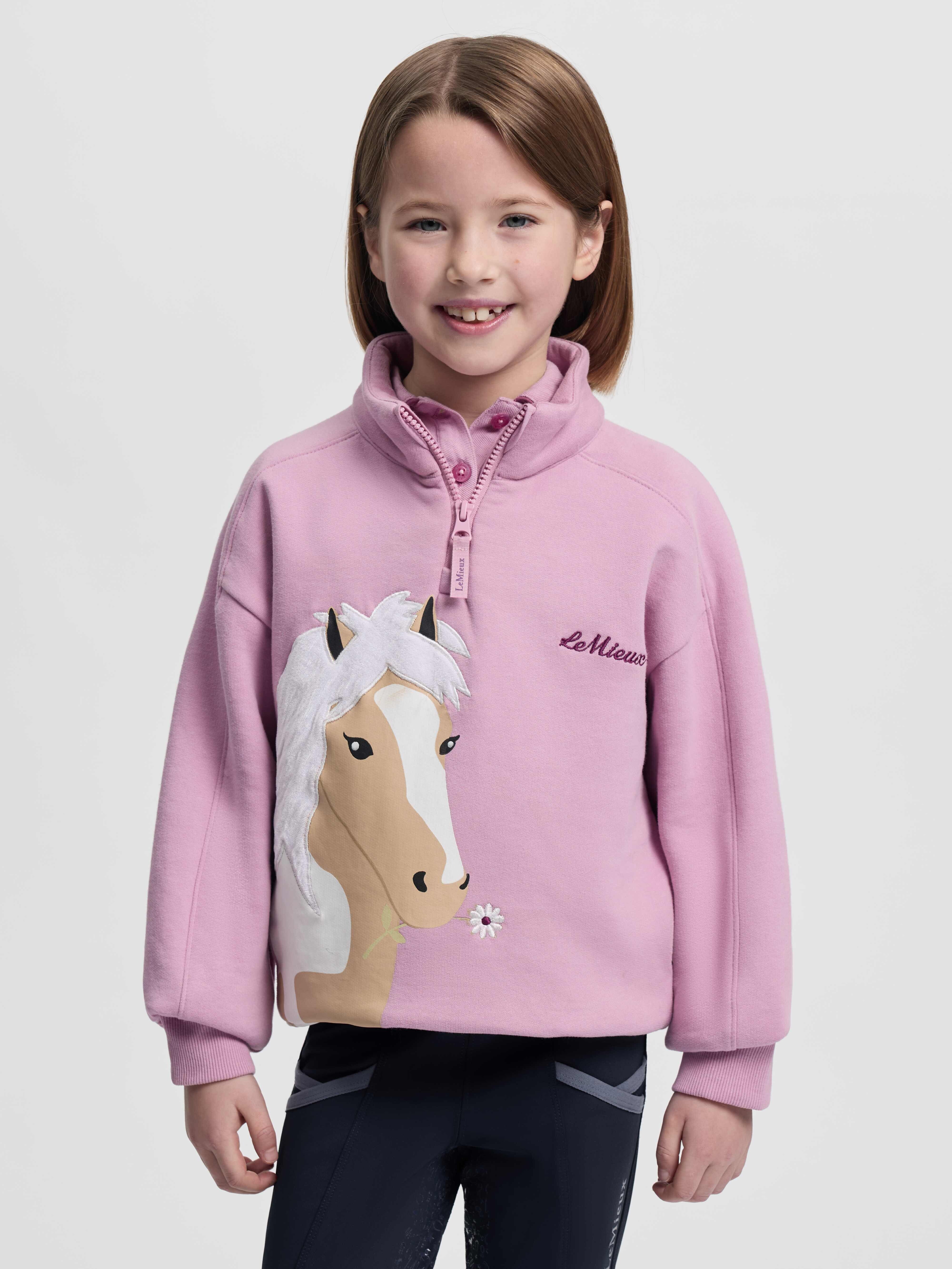 Front view of child model wearing a LeMieux Mini Quinn Quarter Zip Sweatshirt in a pink color with horse head design