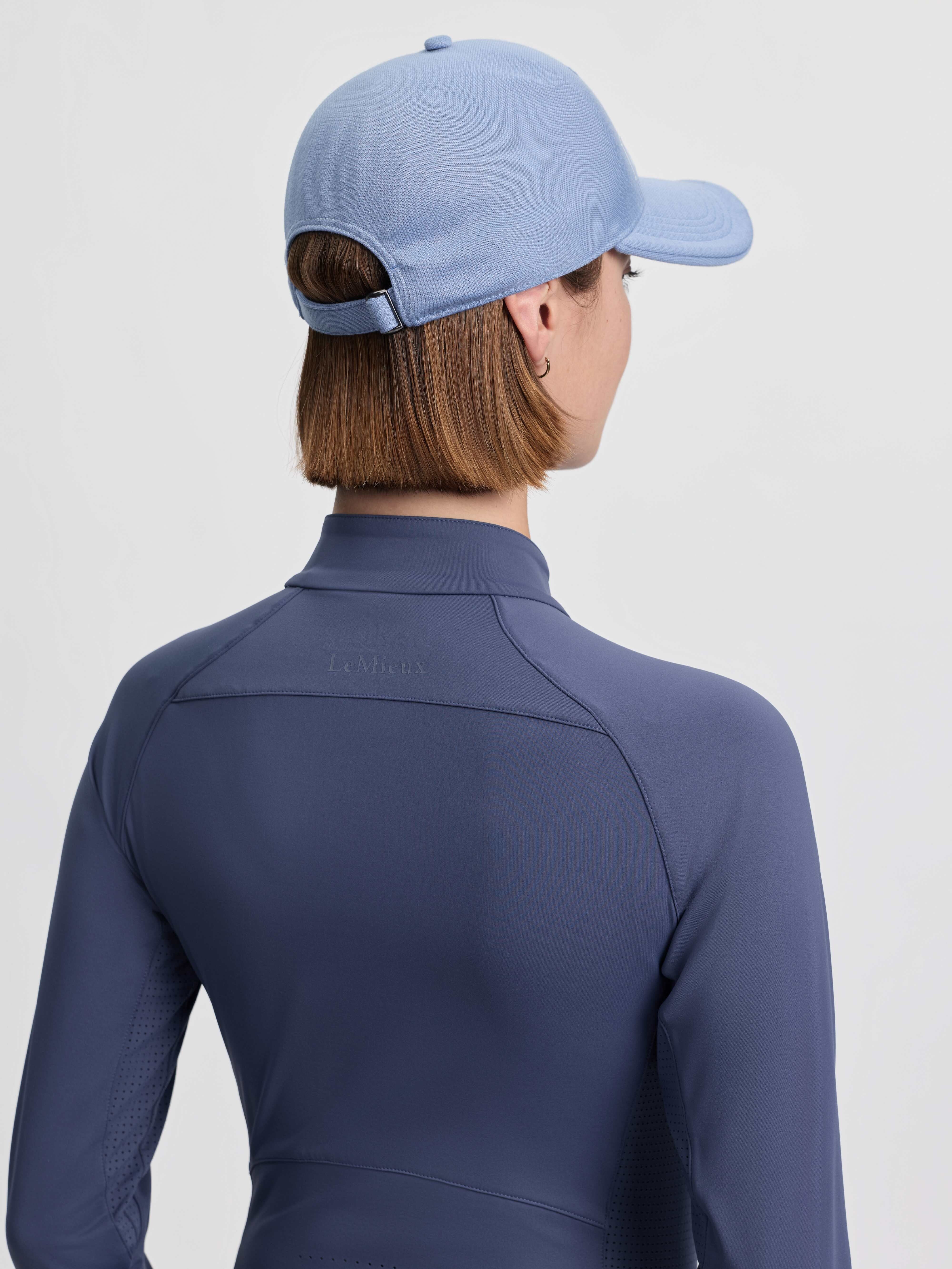 Back view of a female model wearing the powder blue LeMieux Lara Cap on a plain background