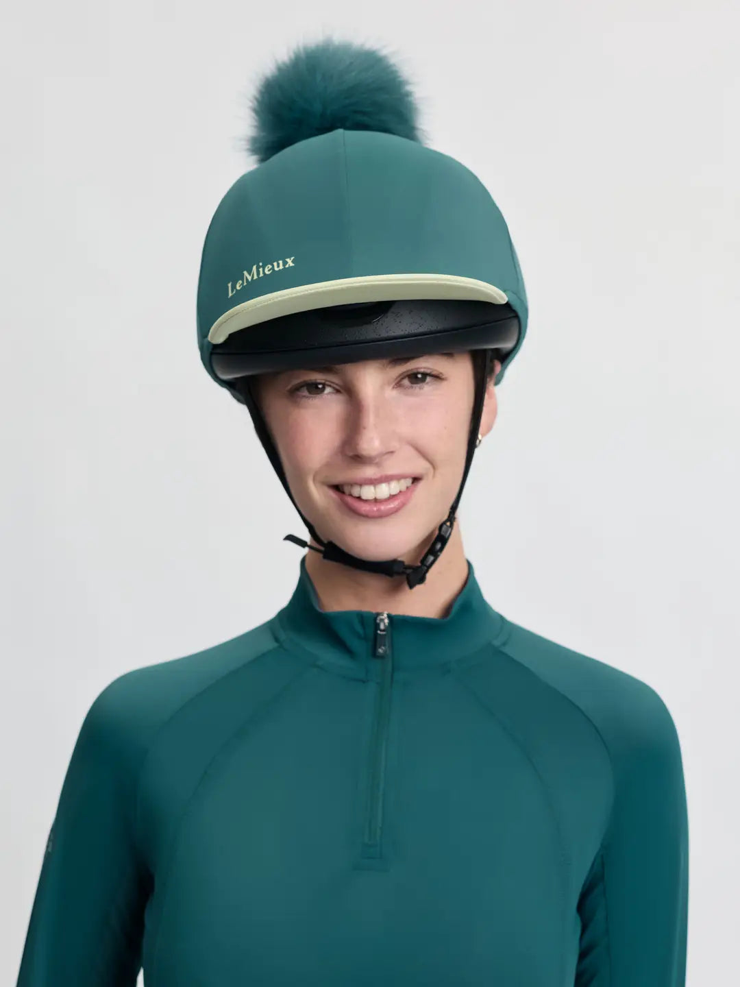 Front view of a female model wearing the green LeMieux Classique Pom Hat Silk on a plain background