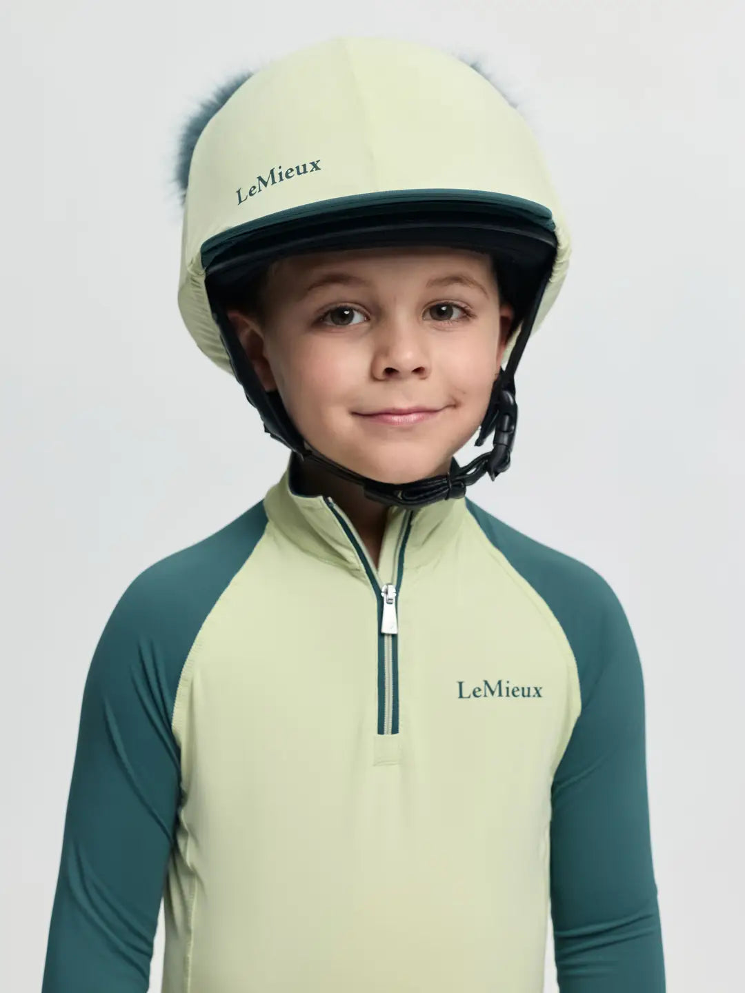 Front view of a young male model wearing the Macaron LeMieux Mini Double Pom Hat Silk on a plain background