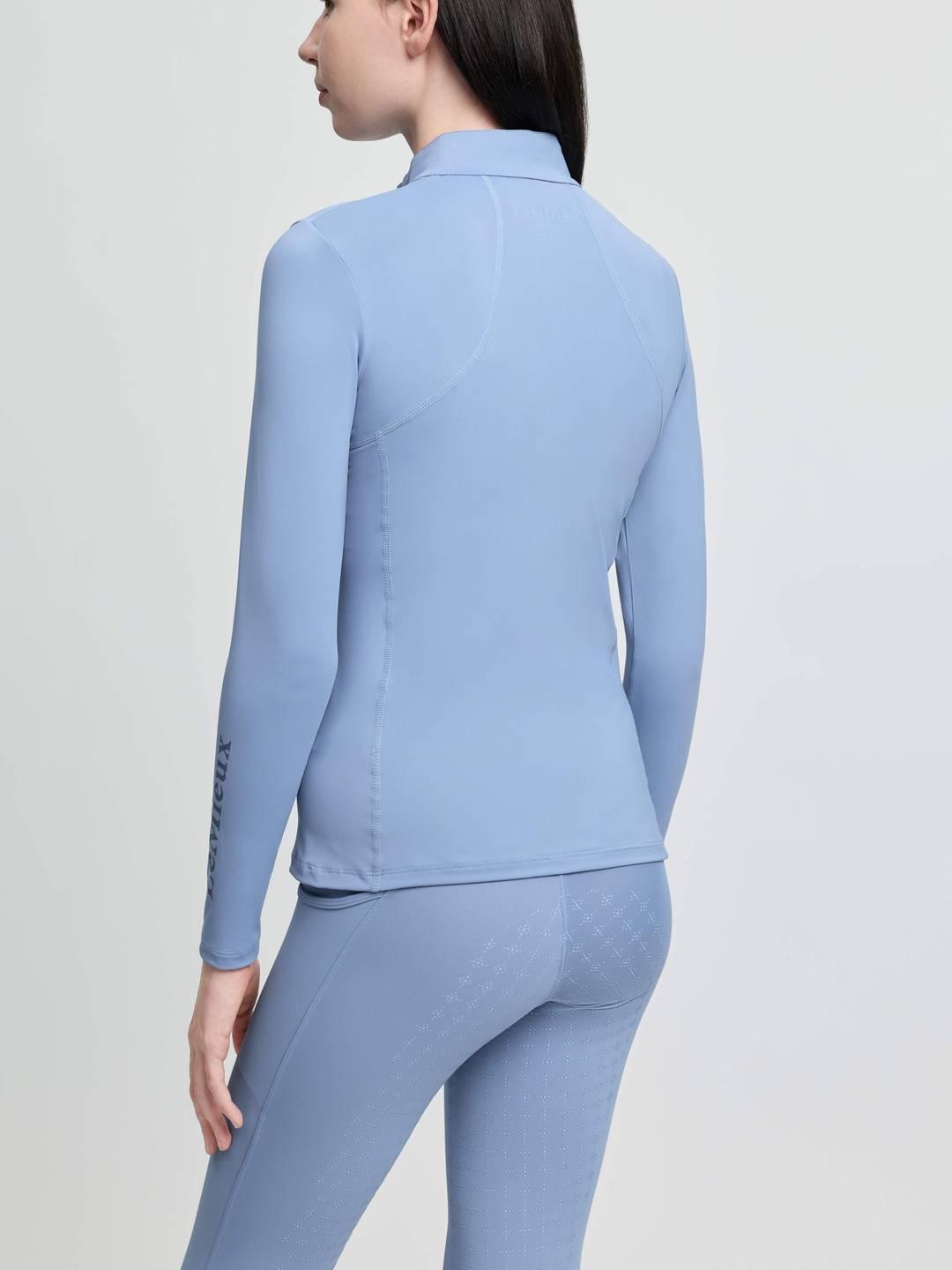 Back view of a young female model wearing the powder blue LeMieux Young Rider Classique Base Layer on a plain background