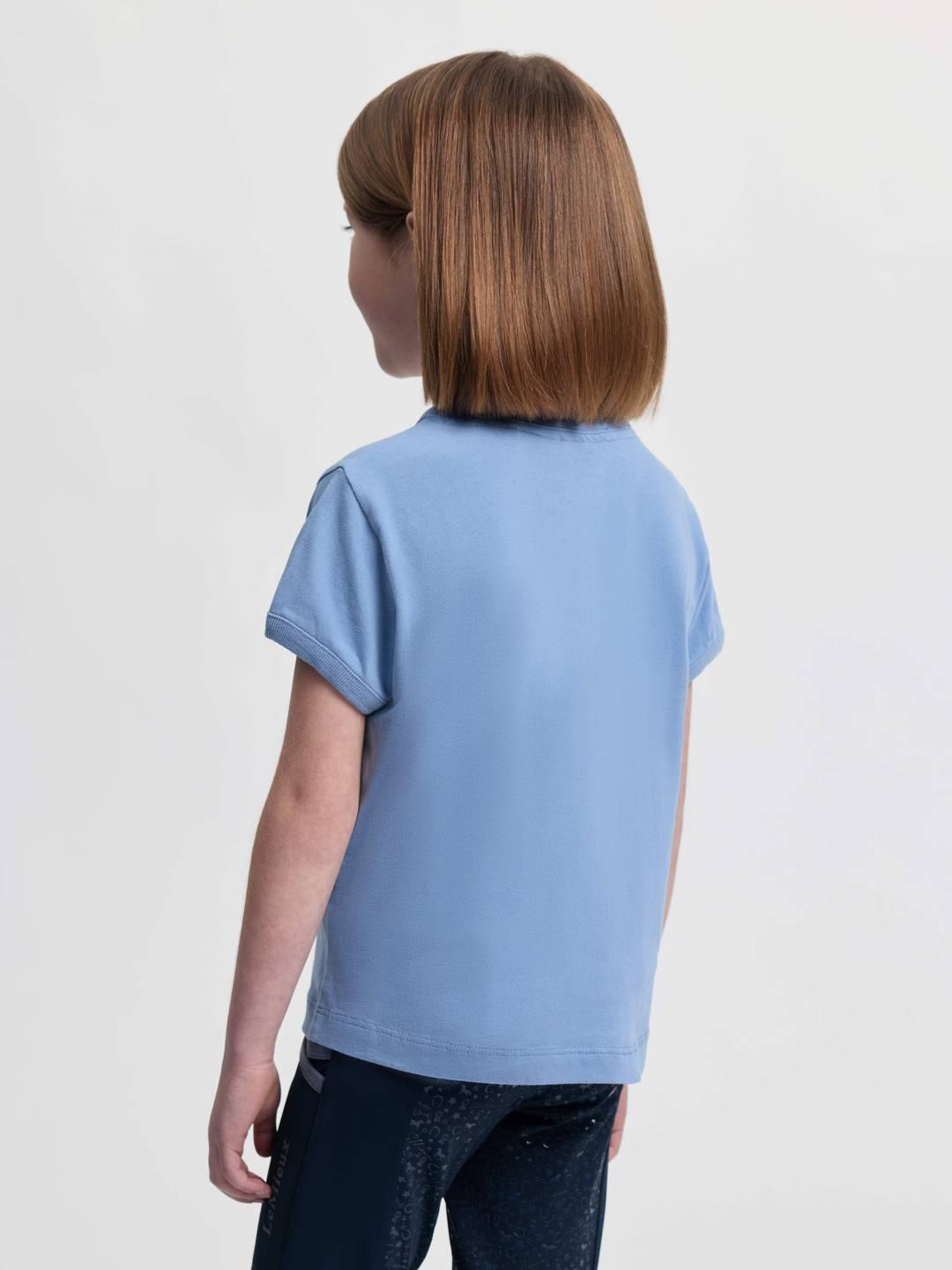 Back view of a young female model wearing the powder blue LeMieux Mini Alex T-Shirt on a plain background