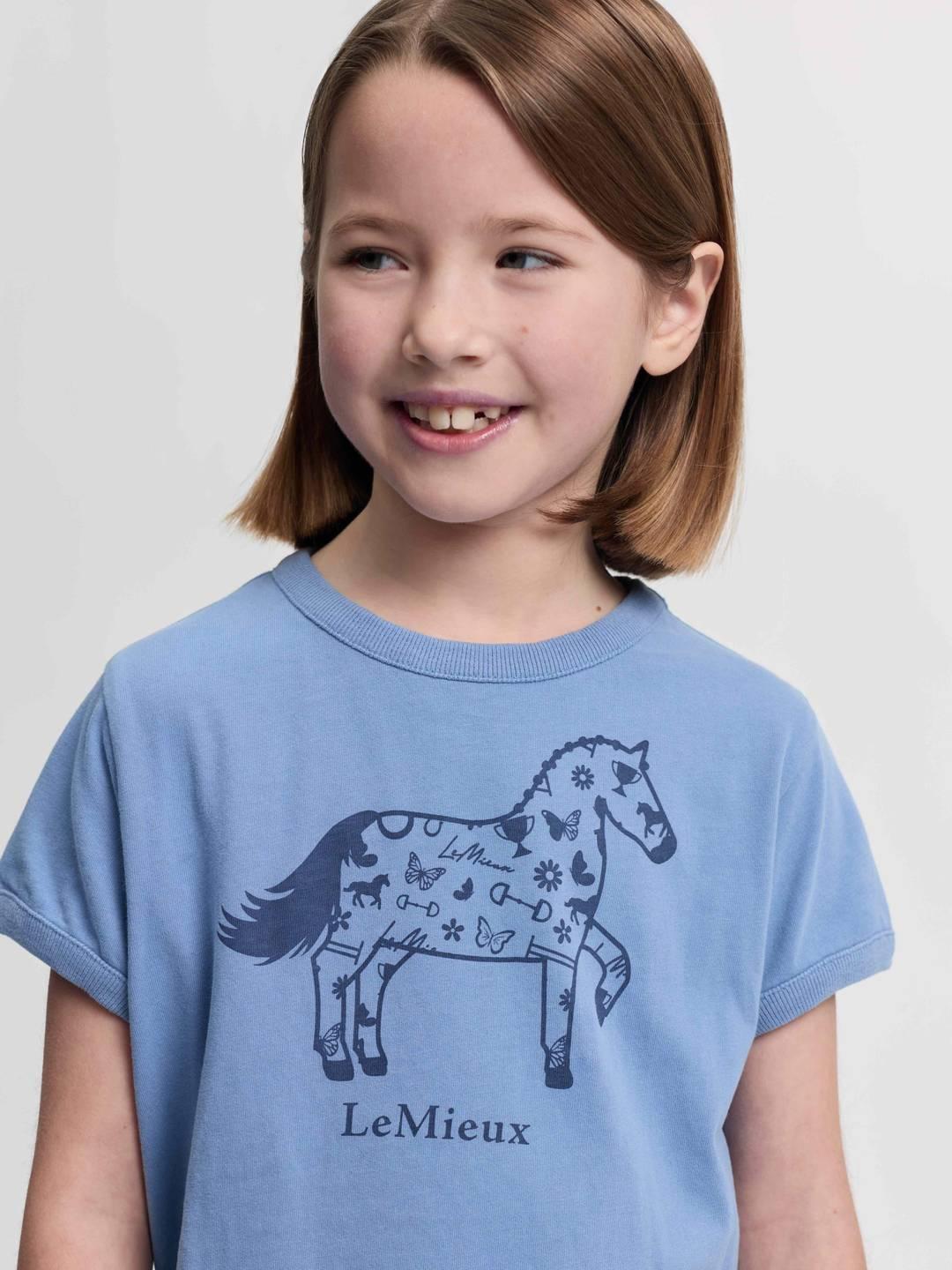 Close-up front view of a young female model wearing the powder blue LeMieux Mini Alex T-Shirt on a plain background