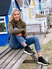 Front view of a female model wearing a pair of black LeMieux Kanta Waterproof Trainers at the beach