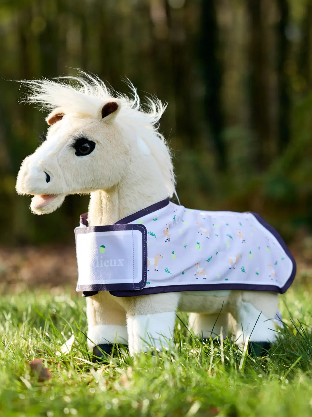 Stuffed animal horse standing outside wearing the LeMieux Toy Pony Lemon Printed Rug in lilac 