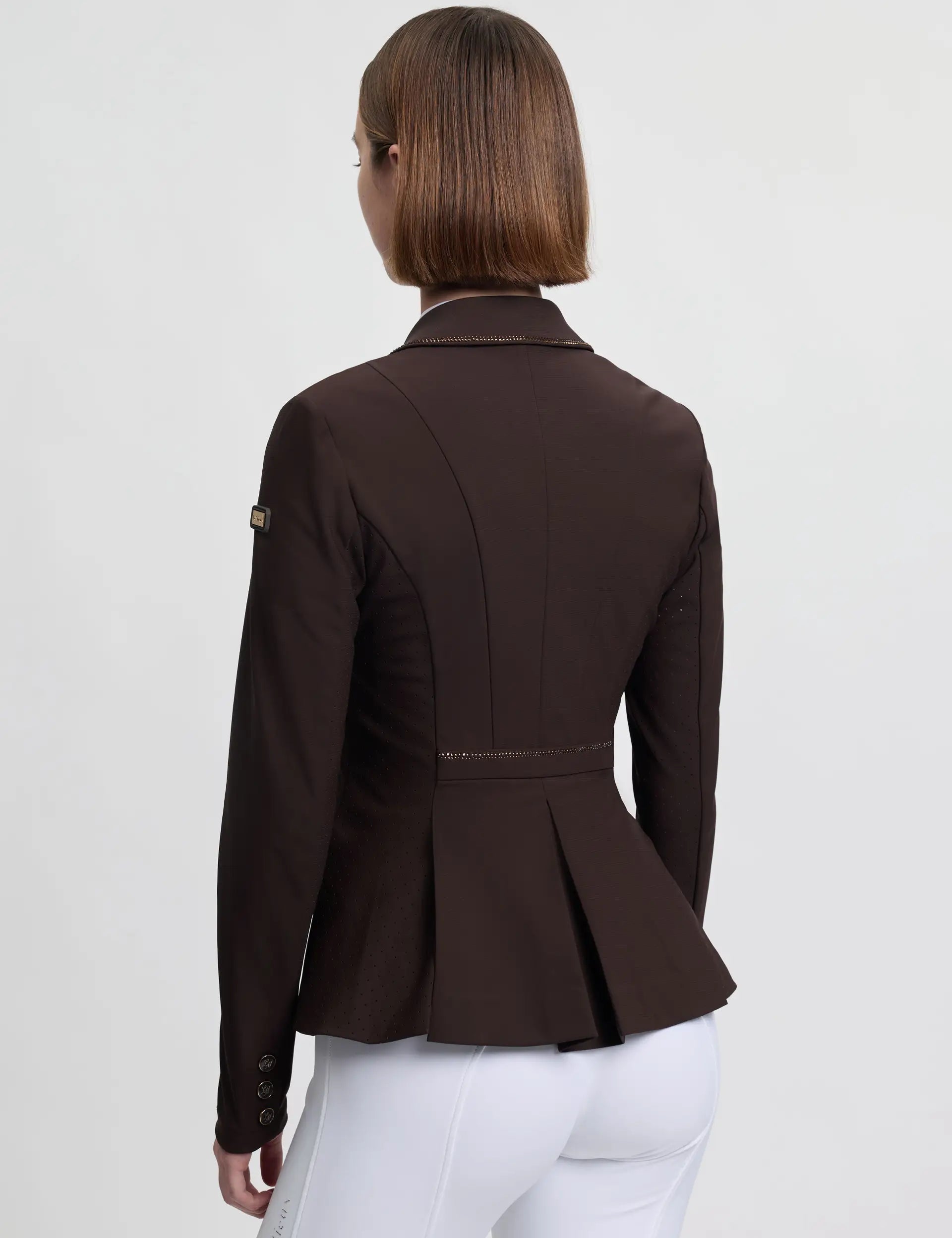 Back view of a female model wearing the brown LeMieux Brilliance Diana Show Jacket on a plain background