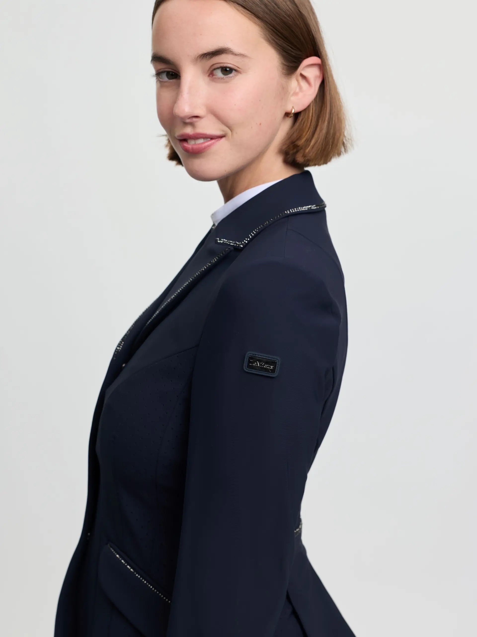 Side view of a female model wearing the navy LeMieux Brilliance Diana Show Jacket on a plain background