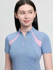Close-up front view of a young female model wearing the blue LeMieux Young Rider Mia Mesh Short Sleeve Base Layer on a plain background
