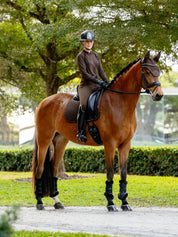 Angled front view of a female model riding a bay horse wearing the brown LeMieux Brilliance Dressage Square and coordinating accessories