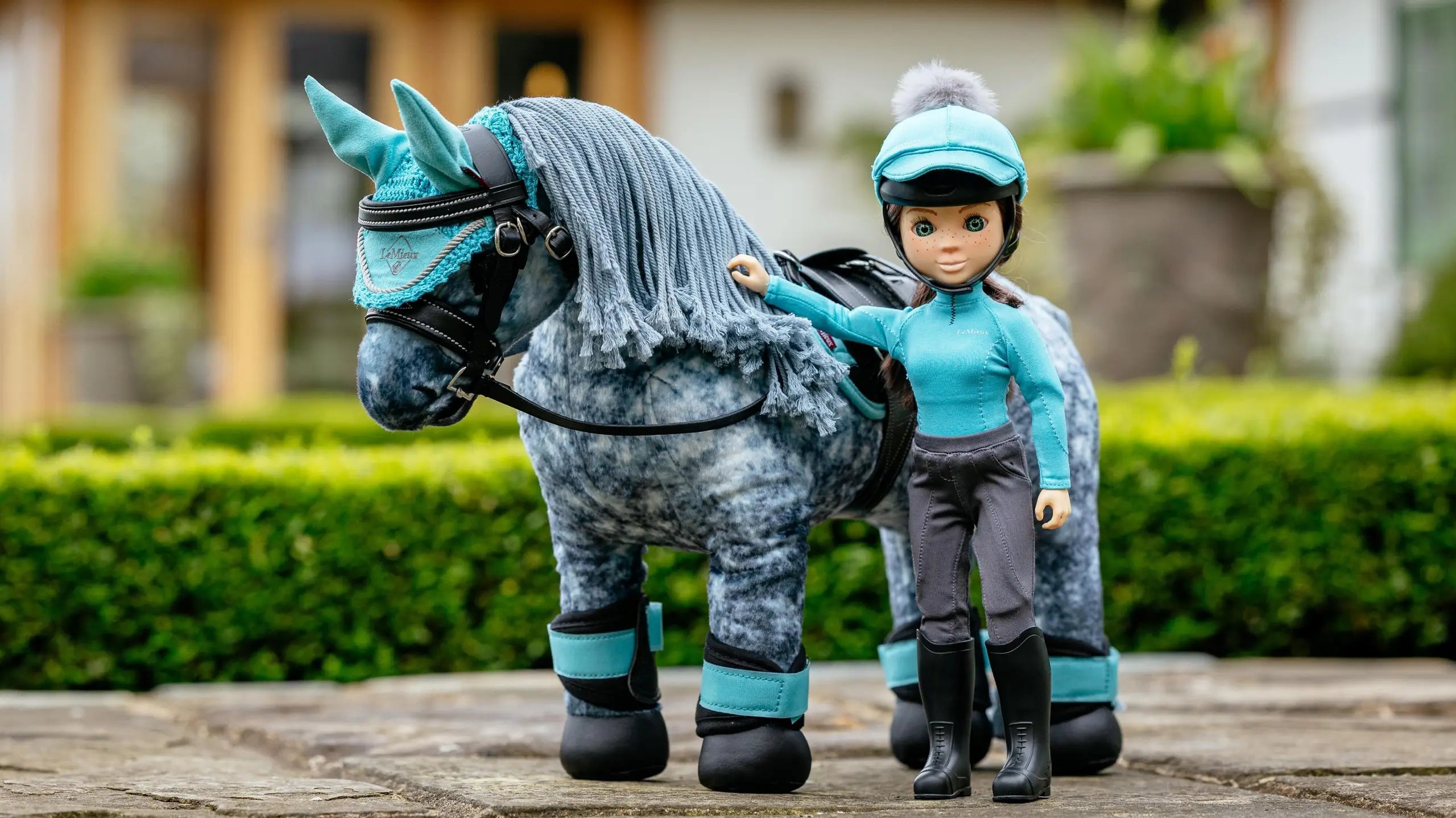 Front view of the blue Florence LeMieux Toy Rider standing next to a gray toy pony outside