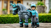 Front view of the blue Florence LeMieux Toy Rider standing next to a gray toy pony outside