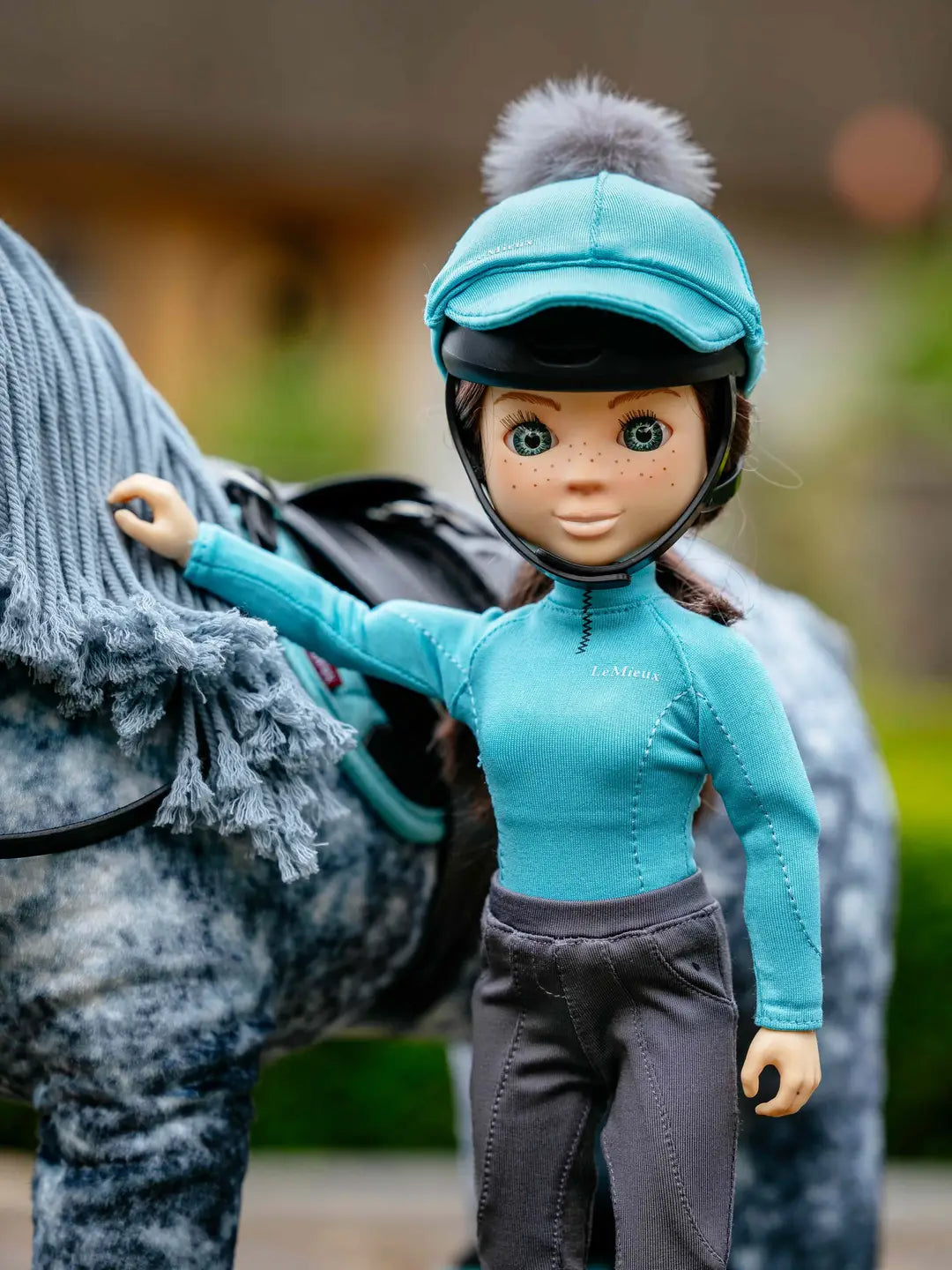 Front view of a toy rider wearing the LeMieux Toy Rider Outfit while standing next to a gray toy pony