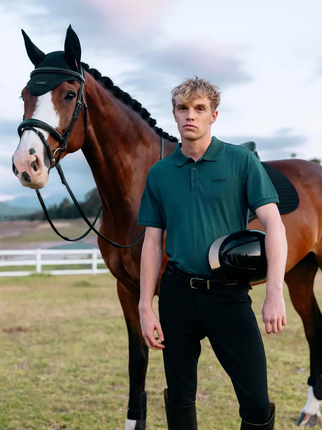 Man wearing LeMieux Men’s Classique Polo Shirt in Jungle green standing beside a horse outdoors