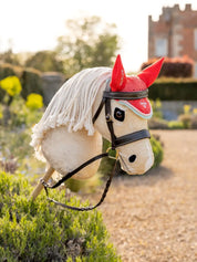 Angled front view of a palomino hobby horse wearing the coral LeMieux Hobby Horse Harlow Fly Hood in a garden setting