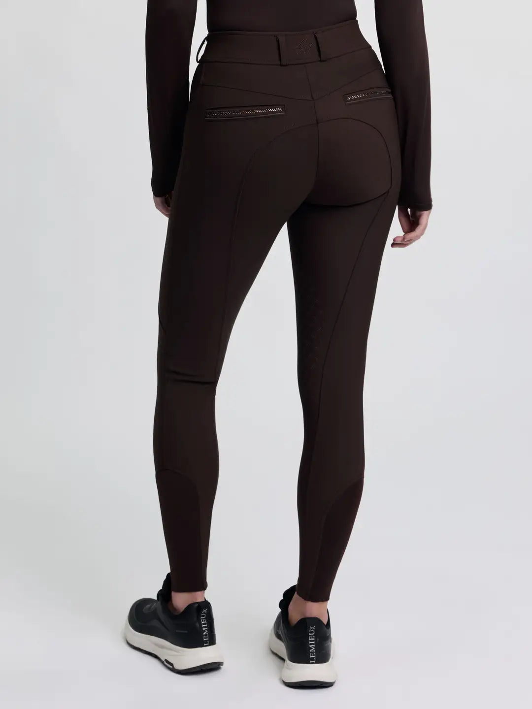 Back view of a model wearing the brown LeMieux Brilliance Knee Grip Breeches on a plain background
