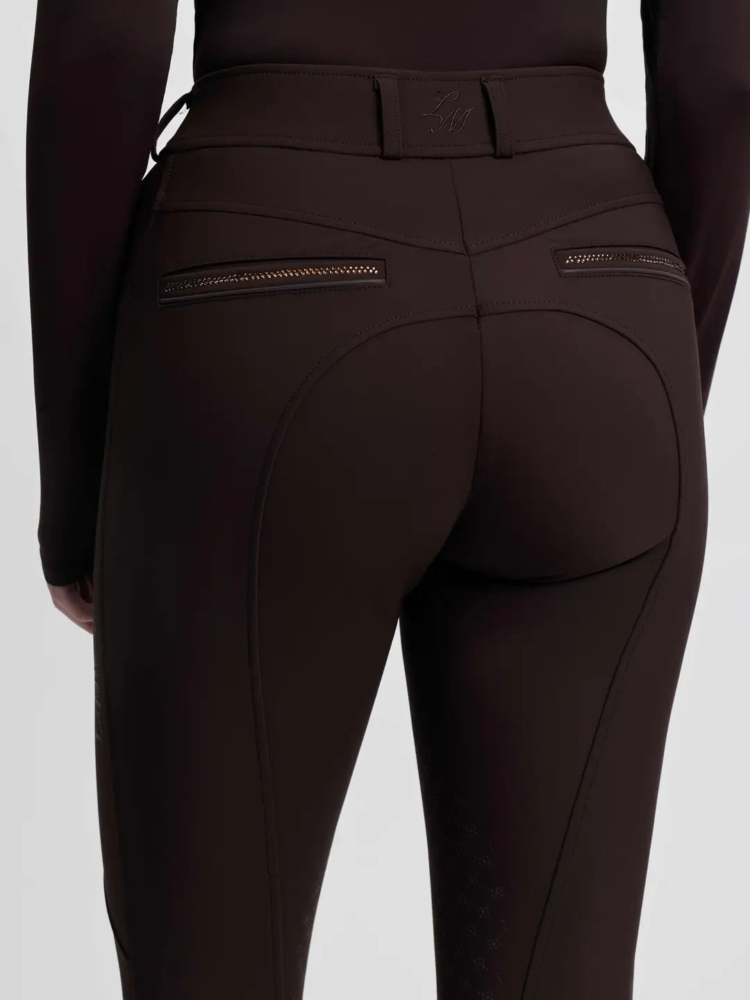 Close-up back view of a model wearing the brown LeMieux Brilliance Knee Grip Breeches on a plain background