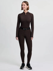 Full body front view of a model wearing the brown LeMieux Brilliance Full Seat Breeches, brown long sleeve shirt, and black tennis shoes on a plain background