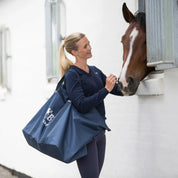View of a woman petting a horse's head while wearing the navy B Vertigo Helsinki Large Travel Bag on her shoulder