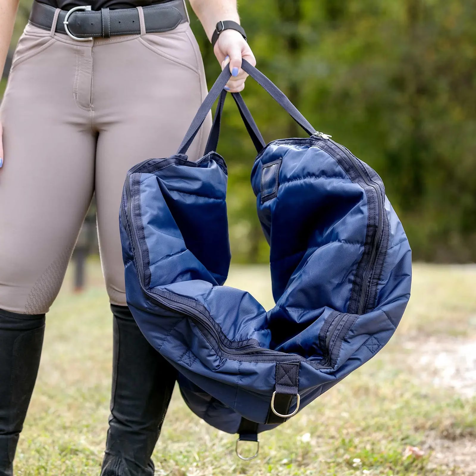Front view of a model standing outside carrying a saddle in the navy Horze Saddle Bag, by the handles