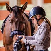 Side view of a female model wearing the Navy/Navy Shimmer Equinavia Crown Glossy MIPS Riding Helmet while standing next to a bay horse