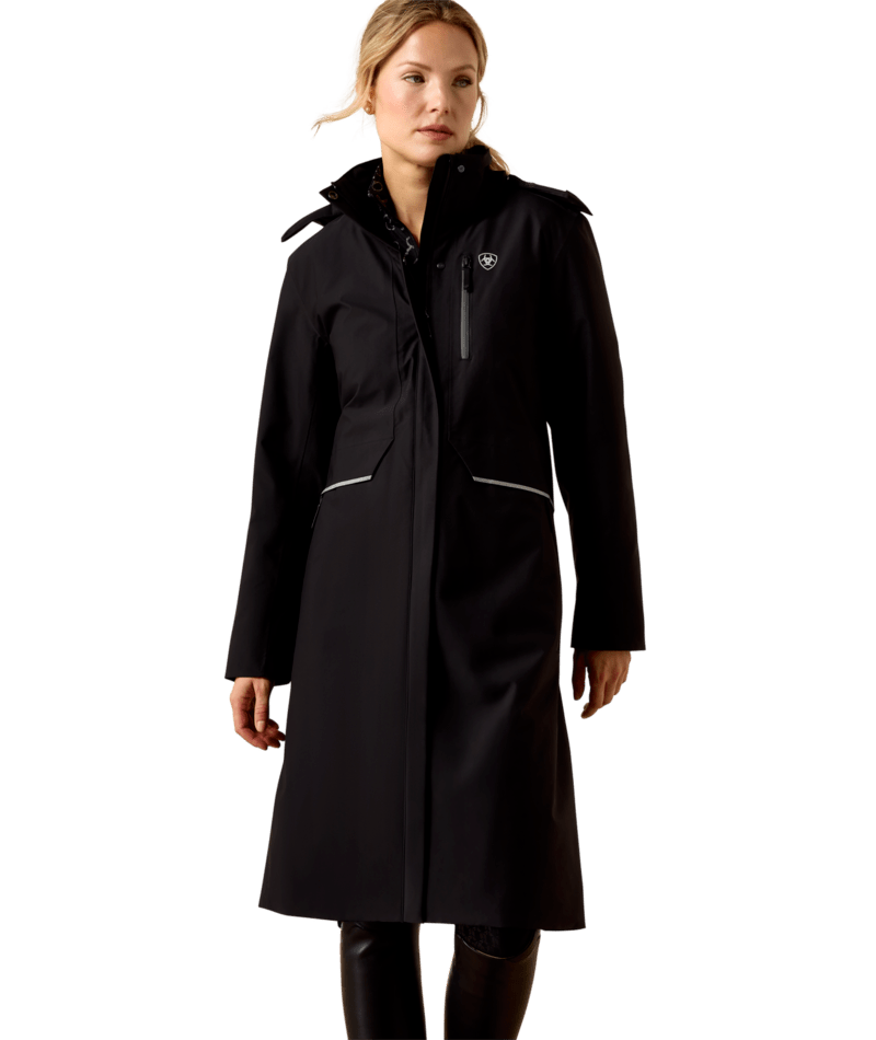 Front view of a female model wearing the Black Ariat Long Rider Waterproof Coat on a white background