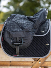 Side view of the black General Purpose LeMieux Ride On Saddle Cover over a saddle sitting on a wood fence.