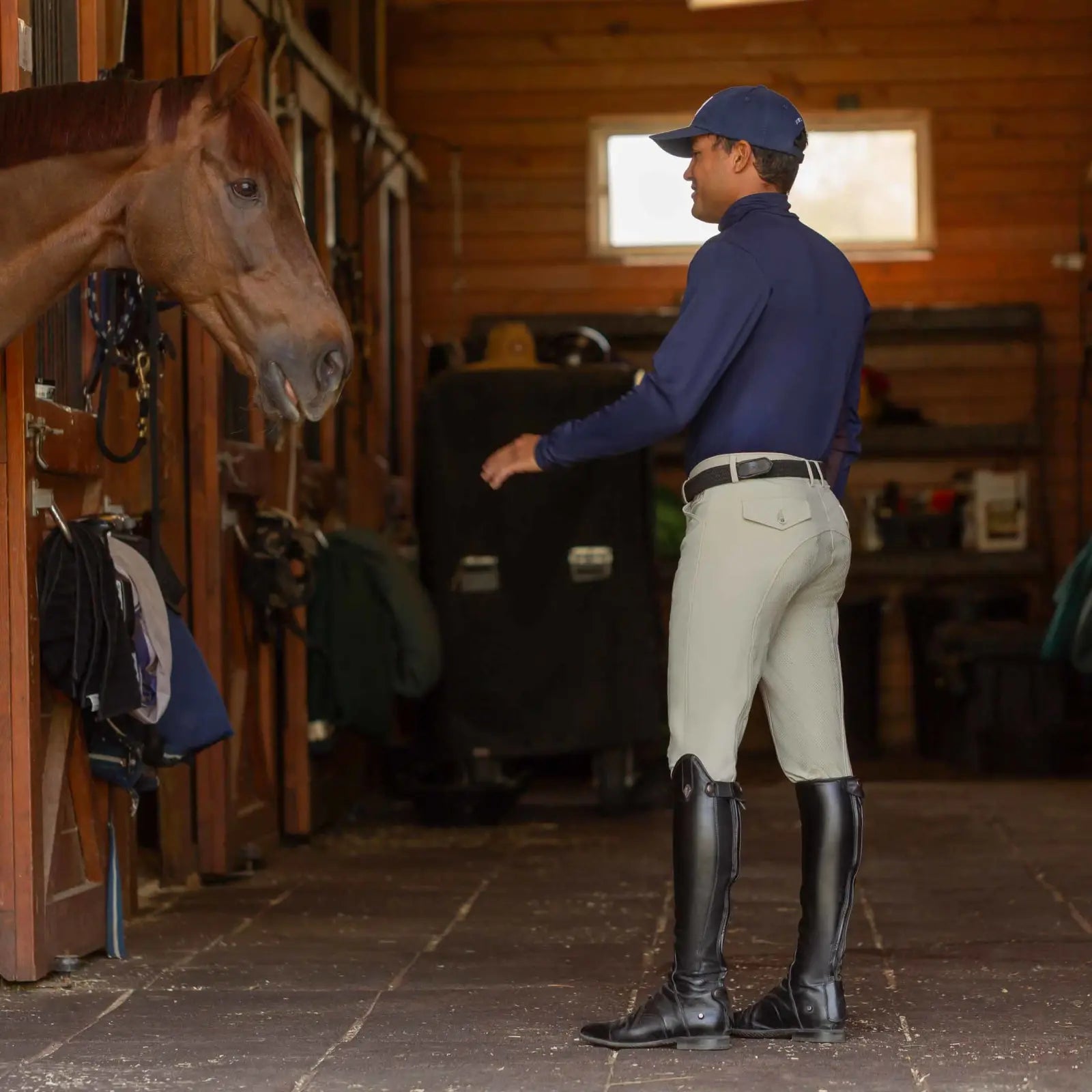 Side view of a model wearing the tan Equinavia Anders Mens Full Seat Breeches while standing in a barn