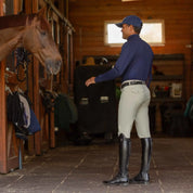 Side view of a model wearing the tan Equinavia Anders Mens Full Seat Breeches while standing in a barn