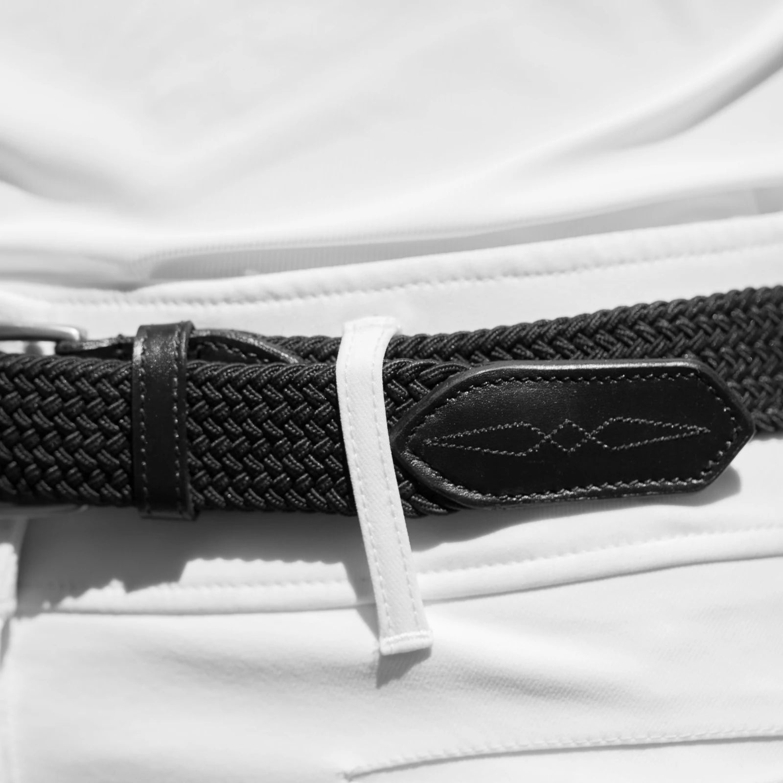 Close-up view of the tail on the black Equinavia Elsa Woven Stretch Belt on a white pair of breeches