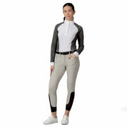 Full body front view of a model wearing the tan Equinavia Kristina Knee Patch Breeches, gray & white show shirt, and white shoes on a white background