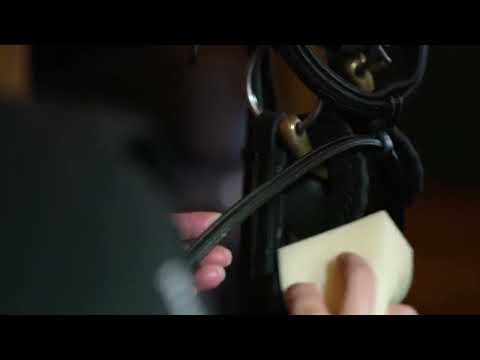 View of someone demonstrating how to use the Carr & Day & Martin Belvoir Tack Cleaner Spray and the Carr & Day & Martin Belvoir Tack Conditioner Spray on tack inside a tack room