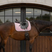 Side view of a bay horse wearing the pink Equinavia Svalbard Dressage Saddle Pad with NordicAir Tech under a saddle while standing in front of barn doors