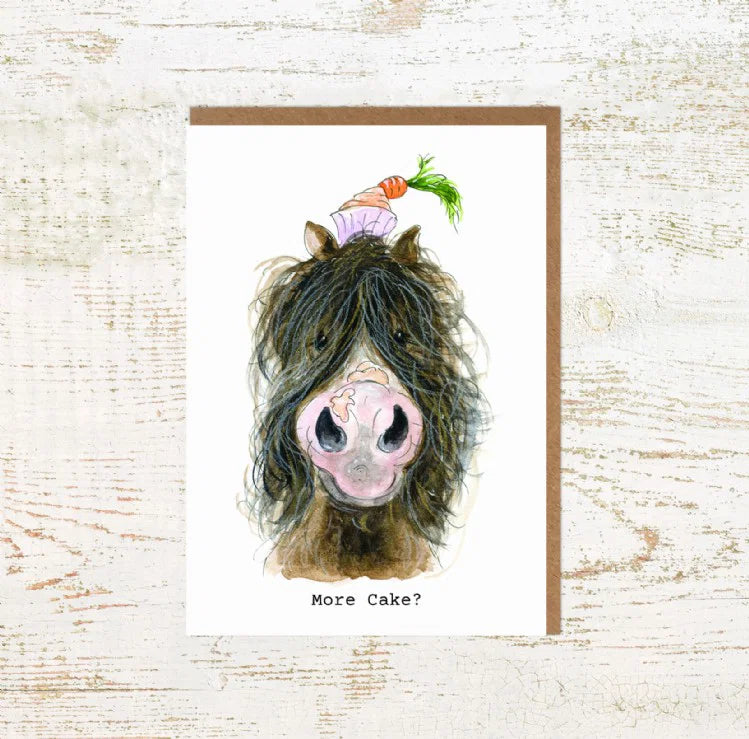 View of the More Cake Pony Pony Nut Greeting Card on a white washed wood background