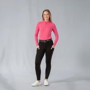Full body front view of a model wearing the Equinavia Kari Womens Long Sleeve Sun Shirt with NordicAir Tech in pink, black breeches, and white sneakers on a gray background