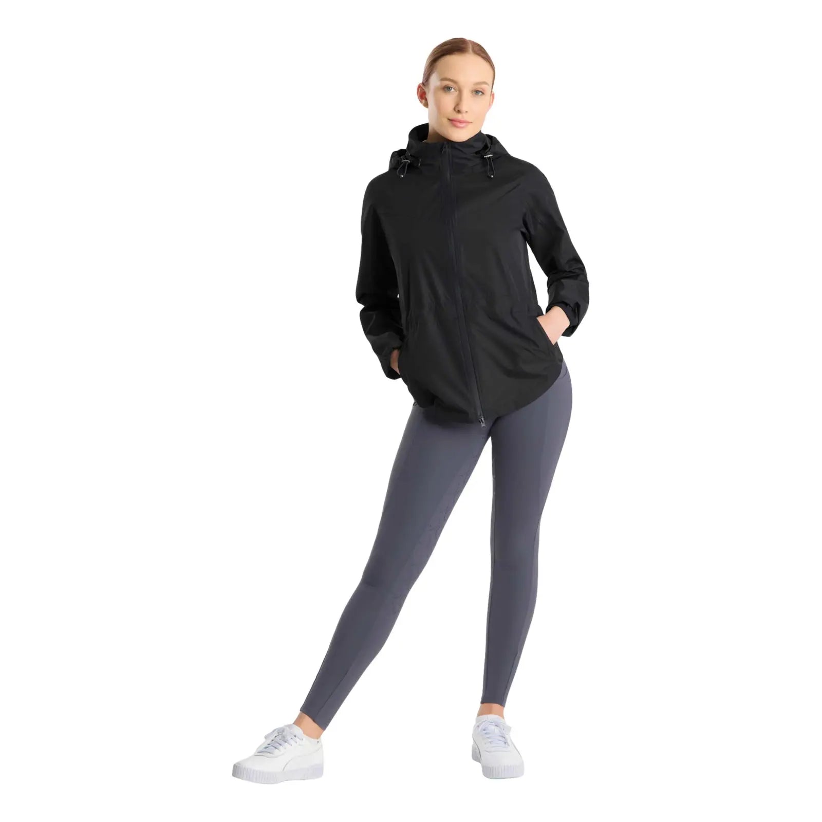 Full body front view of a model wearing the navy Horze Fiora Lightweight Waterproof Jacket, gray tights, and white shoes on a white background
