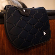 Angled side view of the black embroidered Samshield Spineshield Jump Pad hanging on a tacking stall rail