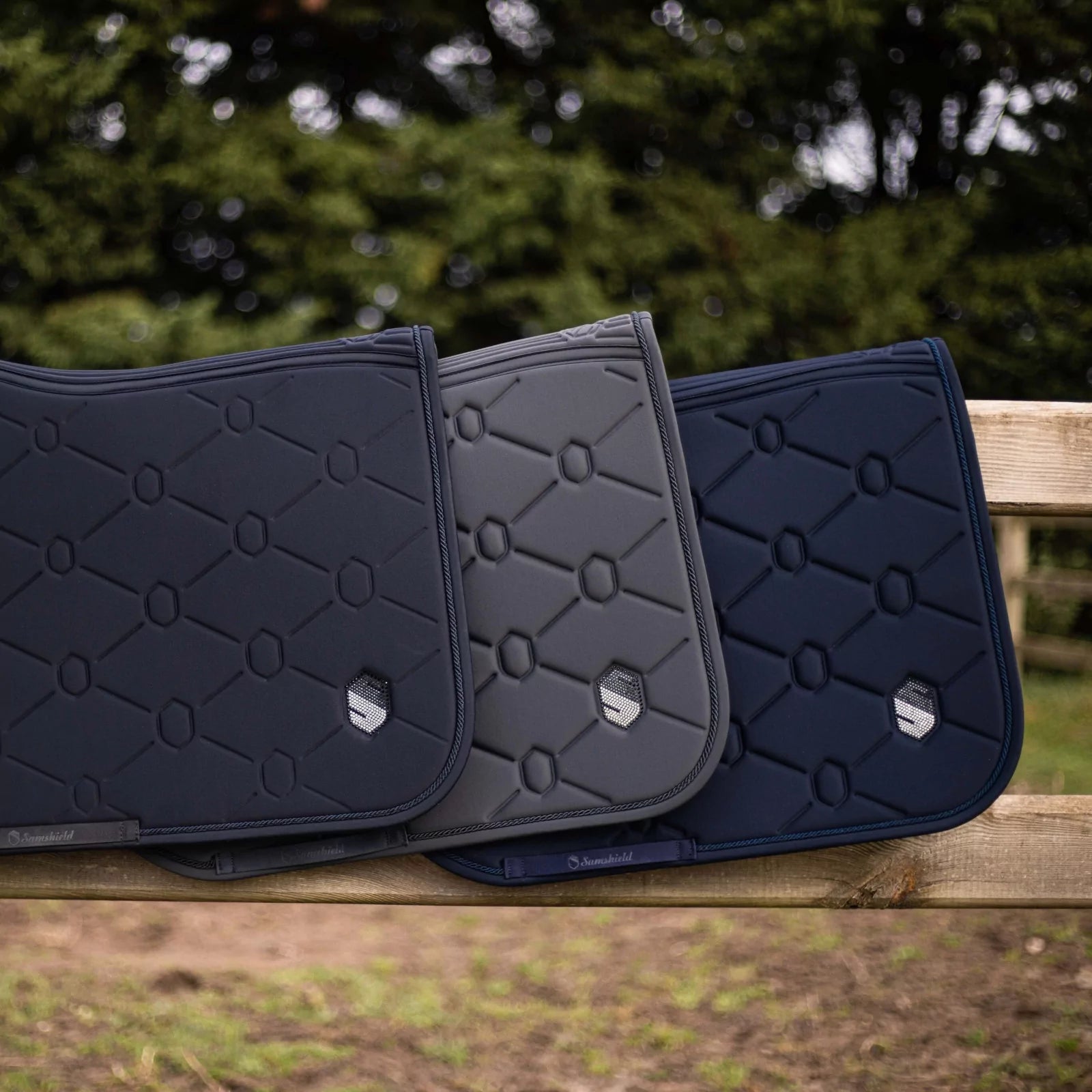 Side view of various colors of the Swarovski Samshield Spineshield Jump Pad  hanging on a wood fence outside